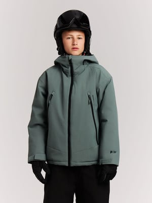 Ein Junge in einer Skijacke und einem Helm mit Brille steht vor hellem Hintergrund. Ein Junge in einer Skijacke und einem Helm mit Brille steht vor hellem Hintergrund.