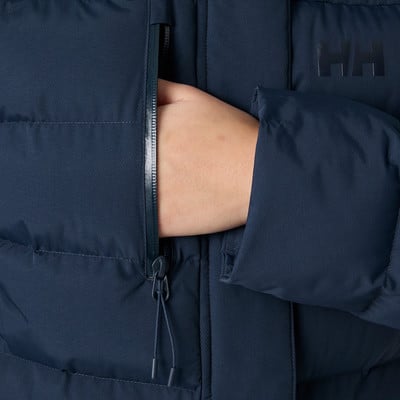 Kéz egy sötétkék HH logós puffer dzseki zsebében. Kéz egy sötétkék HH logós puffer dzseki zsebében.