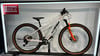 Ein KTM Mountainbike mit weißem Rahmen und orangefarbener Gabel auf einer Ausstellung.