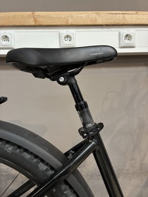 Schwarzer Fahrradsitz mit verstellbarer Sattelstütze und Schutzblech hinten.