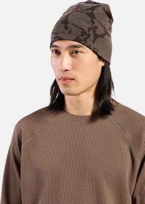 Ein Mann mit langen dunklen Haaren trägt eine braune Mütze und einen Waffelstrickpullover.