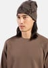 Ein Mann mit langen dunklen Haaren trägt eine braune Mütze und einen Waffelstrickpullover.