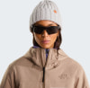 Frau in beige Jacke, lila Pullover und grauer Mütze mit Brille.