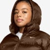 Frau in brauner Daunenjacke mit Kapuze und Nike-Logo.