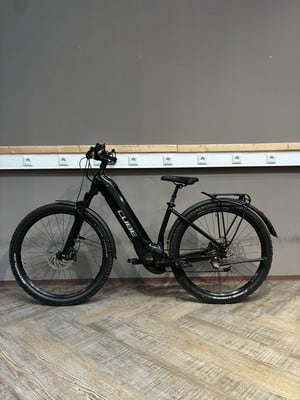 Ein schwarzes Cube E-Bike steht auf einem Holzboden vor einer grauen Wand.