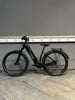Ein schwarzes Cube E-Bike steht auf einem Holzboden vor einer grauen Wand.