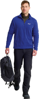 Ein Mann in einem blauen Fleece-Pullover und schwarzer Hose trägt einen Rucksack. Ein Mann in einem blauen Fleece-Pullover und schwarzer Hose trägt einen Rucksack.