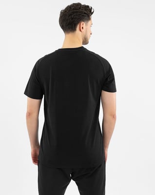 Mann von hinten in einem schwarzen T-Shirt und Jogginghose auf weißem Grund.