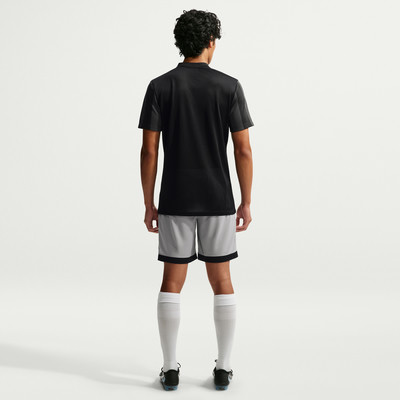 Ein Mann in einem schwarzen Hemd und einer grauen Hose steht mit dem Rücken zur Kamera.