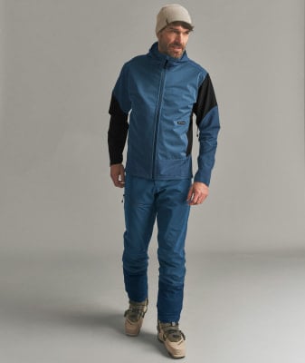 Mann in blauer Skijacke, Hose und Skischuhen auf grauem Hintergrund. Mann in blauer Skijacke, Hose und Skischuhen auf grauem Hintergrund.