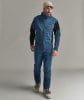 Mann in blauer Skijacke, Hose und Skischuhen auf grauem Hintergrund.