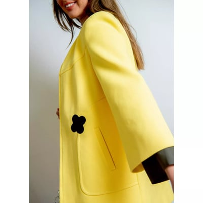 Frau in gelber Jacke mit schwarzer Kleeblatt-Applikation. Frau in gelber Jacke mit schwarzer Kleeblatt-Applikation.