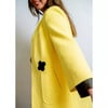 Frau in gelber Jacke mit schwarzer Kleeblatt-Applikation.