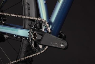 Detail von Kurbel und Kette eines Mountainbikes mit blaugrünem Rahmen.