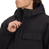 Ein Mann schließt eine schwarze Jacke mit Kapuze und Brusttaschen.