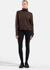 Ein Model in braunem Rollkragenpullover und schwarzer Leggings steht vor weißem Hintergrund.