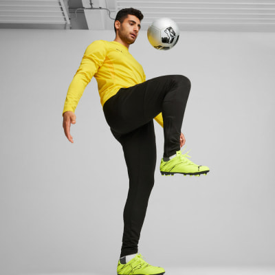 Ein Mann spielt mit einem Fußball, er trägt ein gelbes Sweatshirt und eine schwarze Hose. Ein Mann spielt mit einem Fußball, er trägt ein gelbes Sweatshirt und eine schwarze Hose.