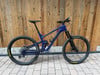 Ein blaues Mountainbike mit Federung steht vor einer Holzwand.