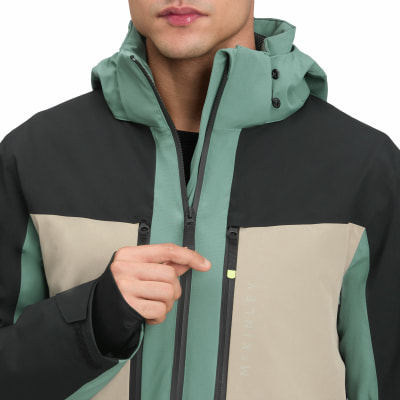 Mann in einer grünen, beige und schwarzen Jacke mit Kapuze und Reißverschluss.