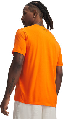 Ein Mann in einem orangefarbenen T-Shirt mit Tätowierungen am Arm und weißen Shorts.