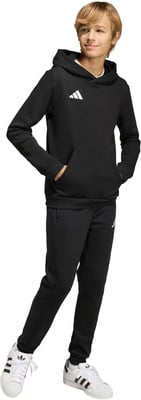 Junge in schwarzer Adidas-Kleidung mit Kapuzenpullover-Tasche und weißen Turnschuhen. Junge in schwarzer Adidas-Kleidung mit Kapuzenpullover-Tasche und weißen Turnschuhen.