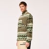 Ein Mann in einem Fleece-Pullover mit ethnischem Muster und grüner Tasche.