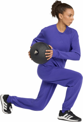 Eine Frau in lila Trainingskleidung hält einen schwarzen Medizinball. Eine Frau in lila Trainingskleidung hält einen schwarzen Medizinball.