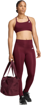Eine Frau in dunkelweinigem Sportoutfit hält eine kleine Tasche. Eine Frau in dunkelweinigem Sportoutfit hält eine kleine Tasche.