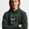 Ein Mann in einem dunkelgrünen Kapuzenpullover mit Nike-Logo auf einem Tennisplatz.