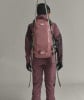 Rückansicht einer Person mit Rucksack und Skiern auf grauem Hintergrund.