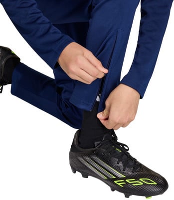 Ein Mann schließt den Reißverschluss an einer dunkelblauen Hose über einem Fußballschuh.