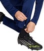 Ein Mann schließt den Reißverschluss an einer dunkelblauen Hose über einem Fußballschuh.