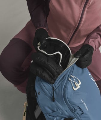 Eine Person packt Skibrille und Handschuhe in einen Rucksack.