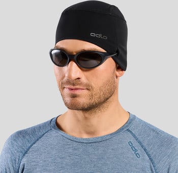 Ein Mann mit schwarzer Mütze und Sonnenbrille auf grauem Hintergrund.