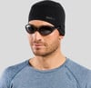 Ein Mann mit schwarzer Mütze und Sonnenbrille auf grauem Hintergrund.