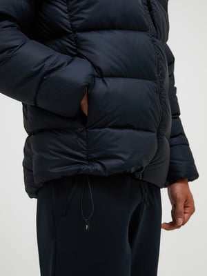 Ein Mann legt seine Hand in die Tasche einer dunklen Daunenjacke.