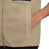 Detail einer gefütterten Weste mit einer Tasche, in die eine Hand greift.