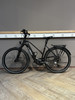 Ein schwarzes KTM E-Bike mit Gepäckträger steht auf einem Holzboden.
