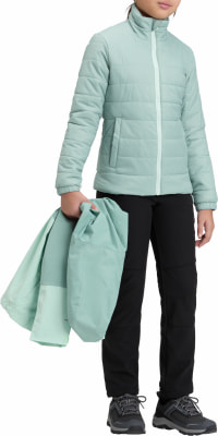 Ein Mädchen hält eine gefaltete hellgrüne Jacke und trägt eine schwarze Jacke und Hose.