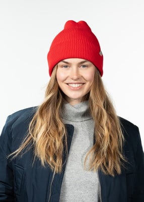 Eine Frau in einer roten Mütze und blauer Jacke lächelt vor weißem Hintergrund.