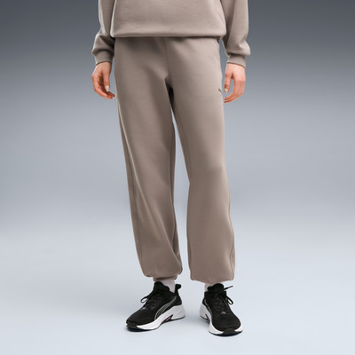 Ein Model in braunen Jogginghosen und schwarzen Turnschuhen posiert vor grauem Hintergrund. Ein Model in braunen Jogginghosen und schwarzen Turnschuhen posiert vor grauem Hintergrund.