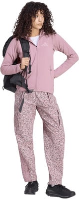 Frau mit lockigem Haar in rosafarbener Jacke und gemusterter Hose mit Rucksack. Frau mit lockigem Haar in rosafarbener Jacke und gemusterter Hose mit Rucksack.