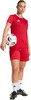 Frau in rotem Trikot hält Fußball, trägt weiße Socken und schwarze Fußballschuhe.