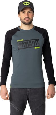 Ein Mann in einem grauen Langarmshirt mit DYNAFIT-Aufdruck und dunkler Jeans. Ein Mann in einem grauen Langarmshirt mit DYNAFIT-Aufdruck und dunkler Jeans.