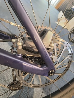 Detail einer hinteren Bremsscheibe und eines Schaltwerks an einem dunkelblauen Fahrrad.