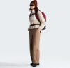 Eine Frau in einem beigen Fleece-Pullover, brauner Hose und mit einem Rucksack.