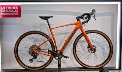 Ein orangefarbenes Cannondale Gravelbike mit schwarzem Lenker und braunen Felgen. Ein orangefarbenes Cannondale Gravelbike mit schwarzem Lenker und braunen Felgen.