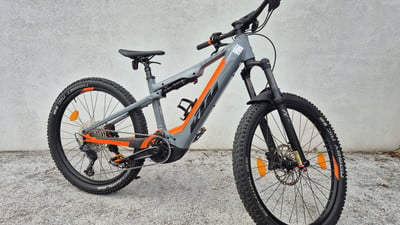 Ein graues KTM E-Bike mit orangefarbenen Akzenten steht auf Beton. Ein graues KTM E-Bike mit orangefarbenen Akzenten steht auf Beton.