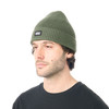 Ein Mann in einer grünen Strickmütze mit 'PICTURE'-Logo vor weißem Hintergrund.