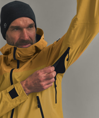 Ein Mann in einer gelben Jacke und schwarzer Mütze öffnet einen Reißverschluss am Ärmel. Ein Mann in einer gelben Jacke und schwarzer Mütze öffnet einen Reißverschluss am Ärmel.